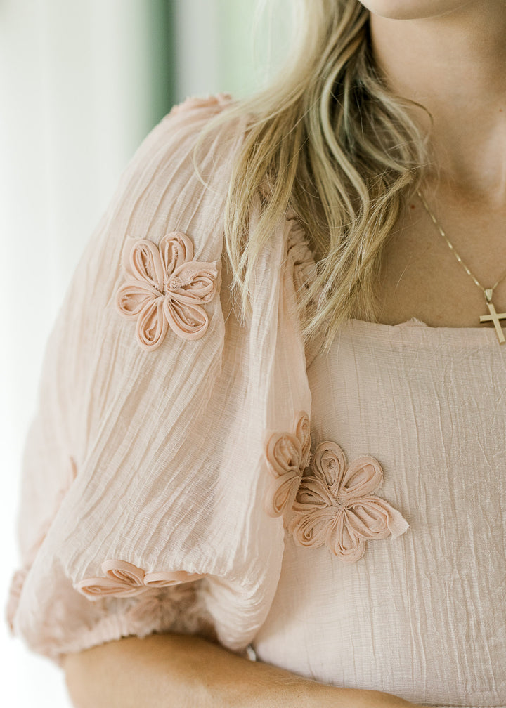 Close up of slightly sheer short sleeve, tulle textured flowers and square neck on pink dress.