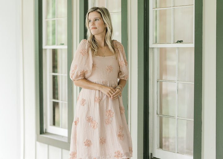 Model wearing a peach above the knee dress with elastic at waist and bubble short sleeves. 