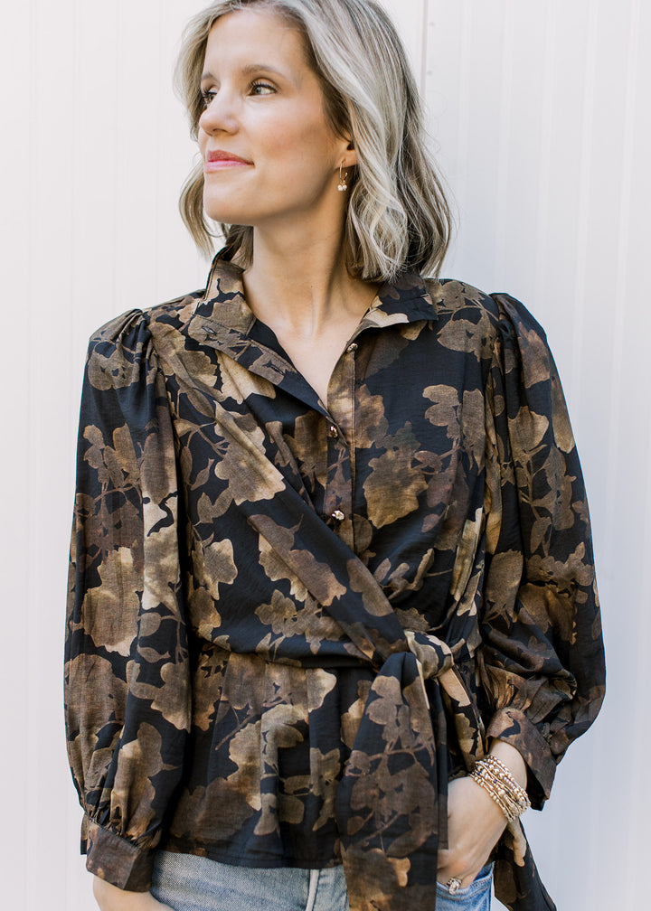 Model wearing a black long sleeve top with brown floral, gold buttons and side tie at the waist.