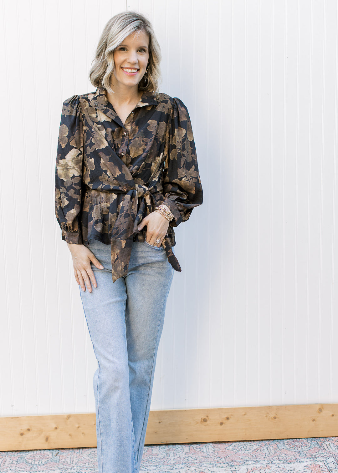 Model wearing jeans and a black long sleeve top with brown floral, gold buttons and tie waist.