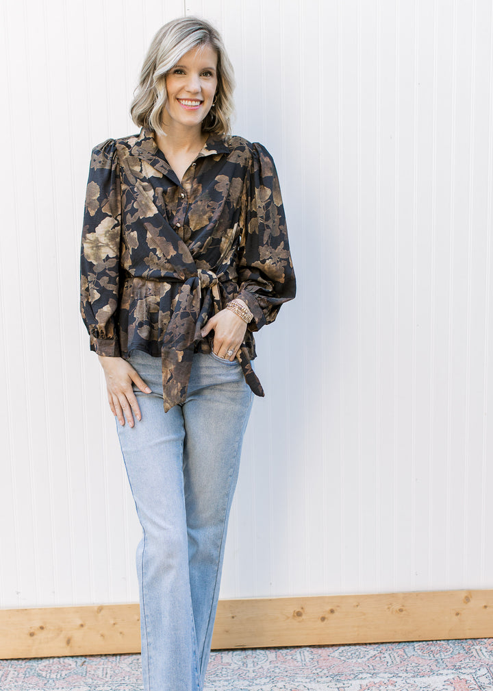 Model wearing jeans and a black long sleeve top with brown floral, gold buttons and tie waist.