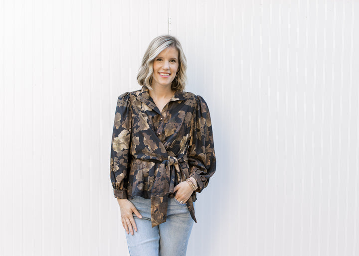 Model wearing a black peplum top with brown floral print, gold buttons and side tie at the waist.
