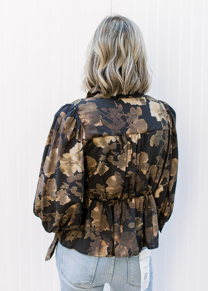 Back view of Model wearing a black peplum top with brown floral print and long sleeves. 