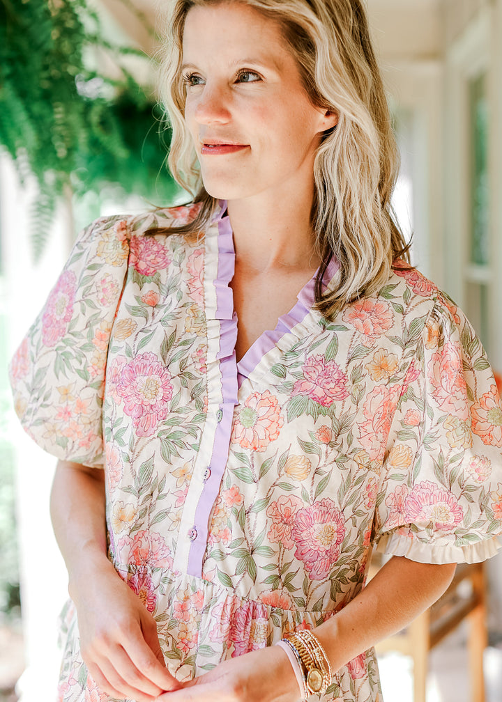 Close up of model wearing a cream dress with floral print, short puff sleeve and v-neck with ruffle.