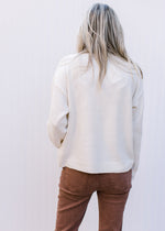 Back view of Model wearing a cream sweater with a gold sequin bow and long sleeves.