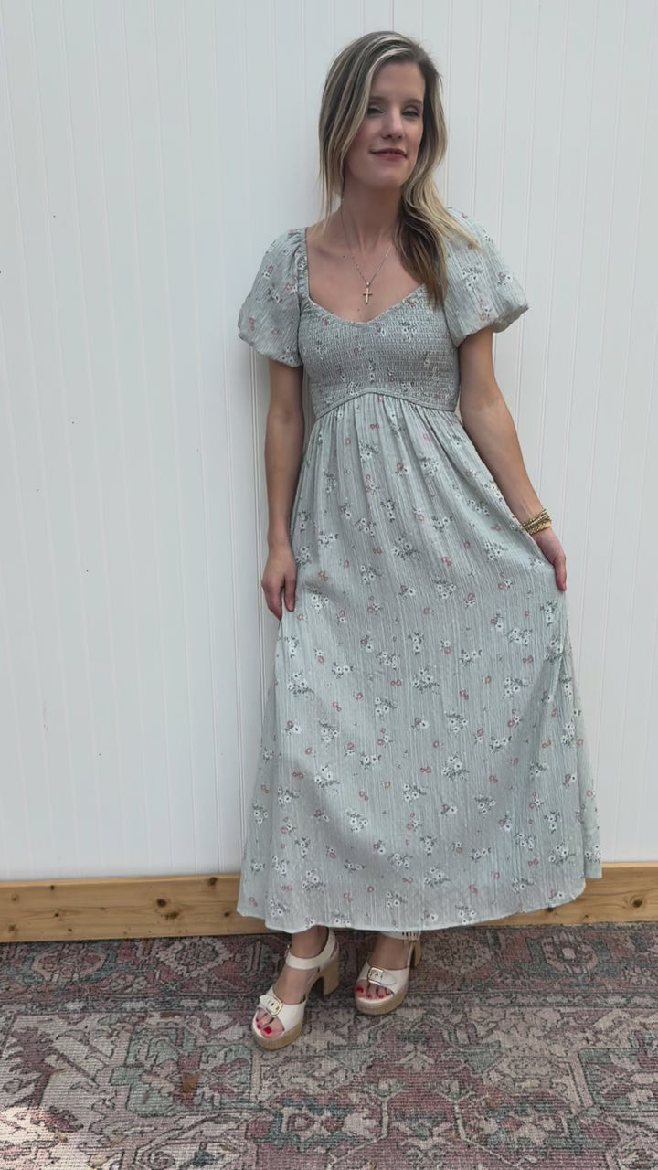 Video of Model wearing a baby blue maxi with peach and cream floral print and a smocked bodice. 