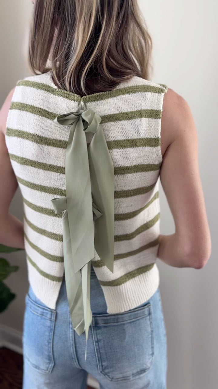Video of Model wearing a sleeveless cream top with sage stripes and open back with tie closure.