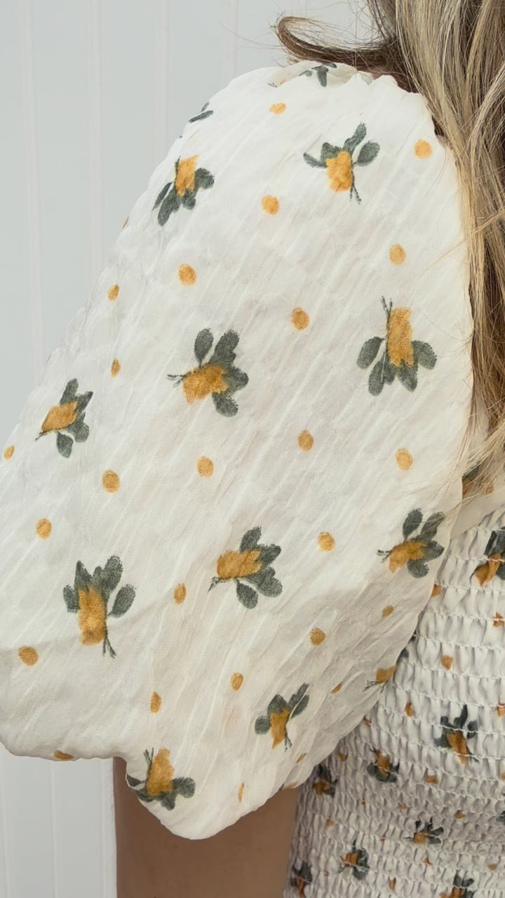 Video of Model wearing a cream maxi with yellow floral, smocked bodice, v-neck and short sleeves. 