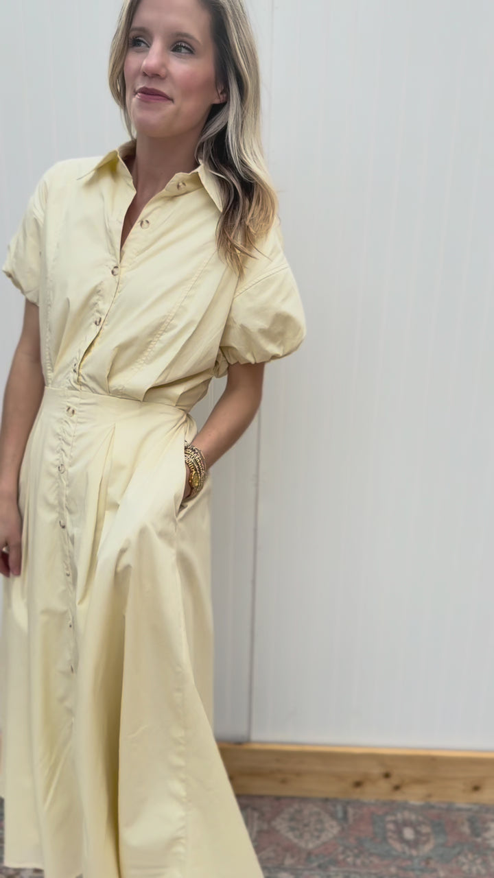 Video of Model wearing a soft yellow midi with a button-front, elastic waist with tie and short sleeves.