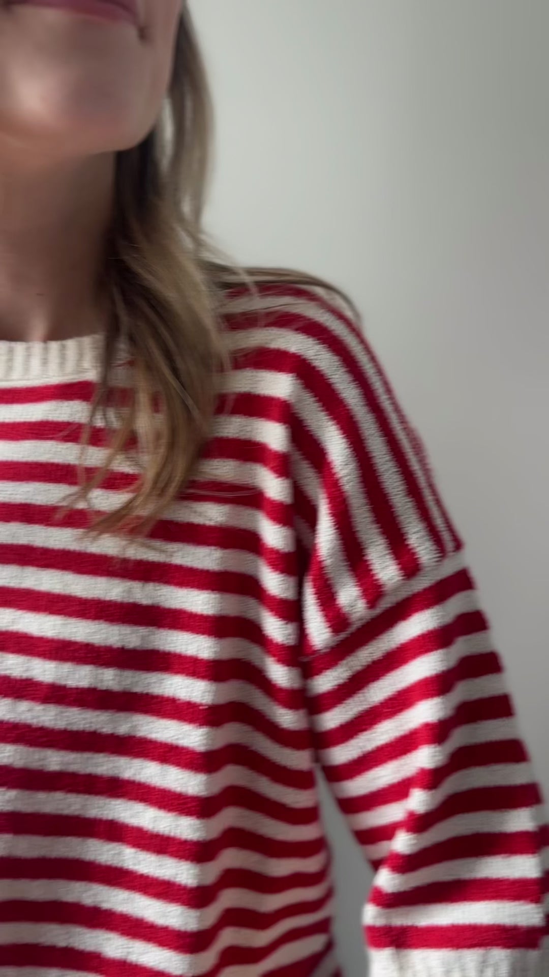 Video of Model wearing a red and white striped knit sweater with short sleeves and button back. 