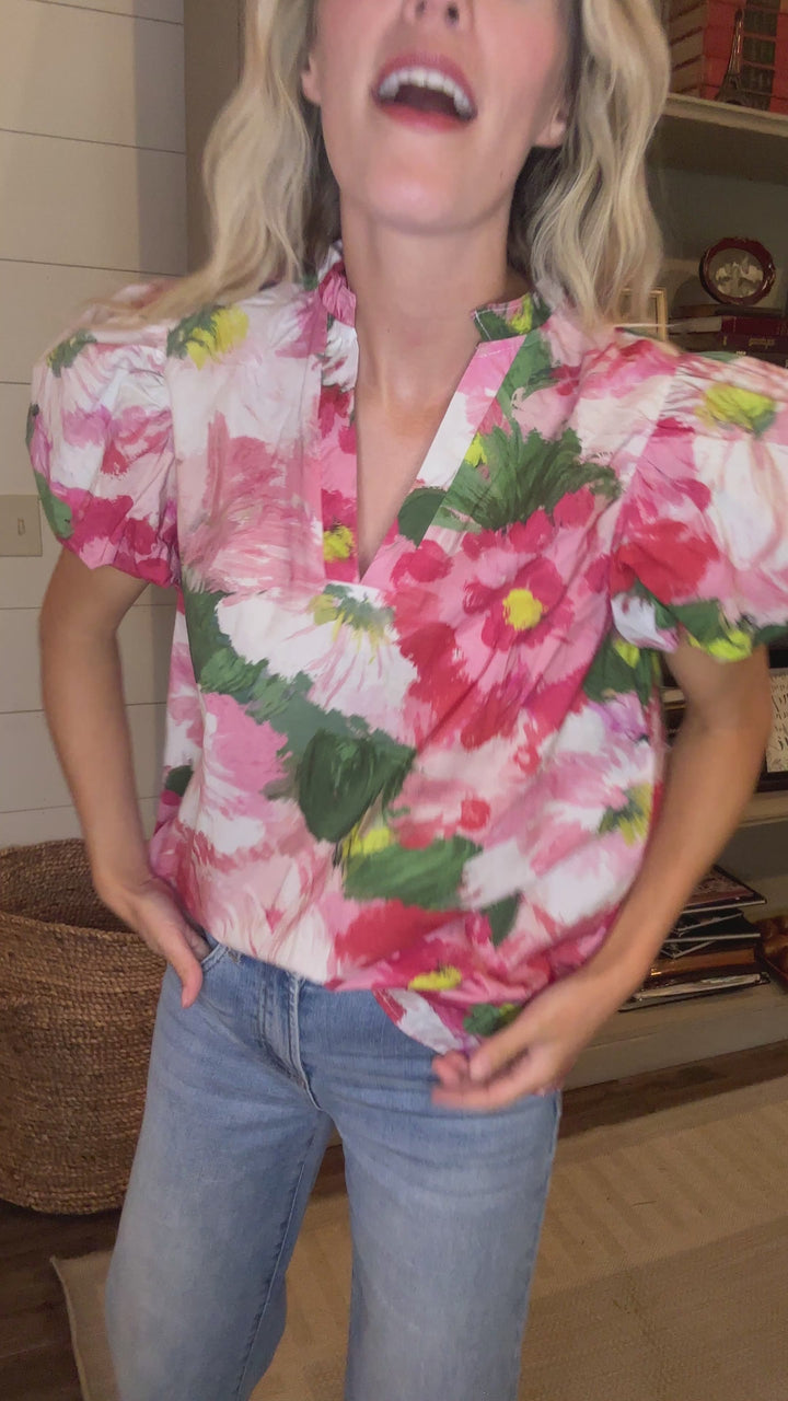 Video of Model wearing a watercolor floral print top with short bubble sleeves and v-neck with ruffle.