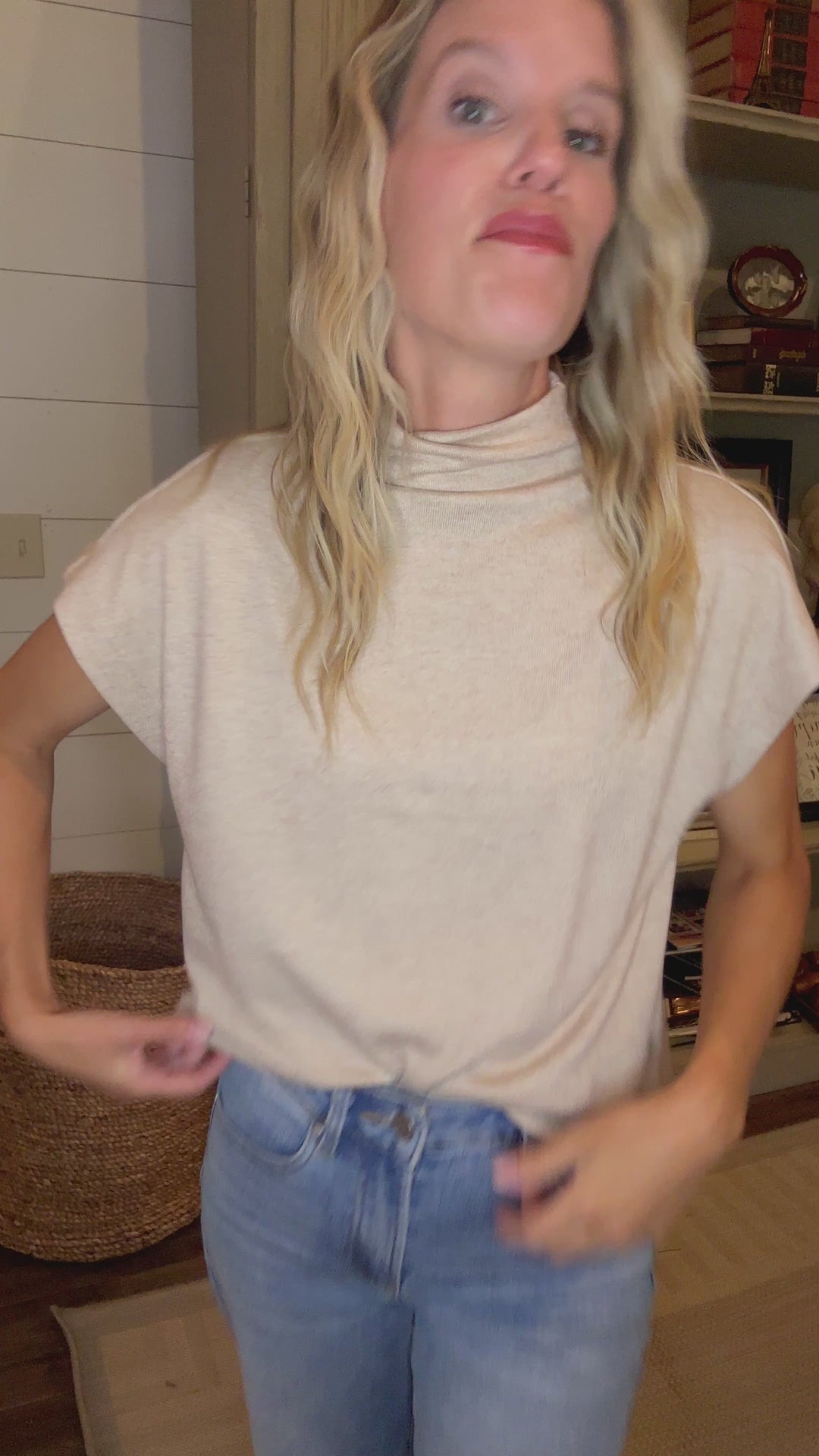 Video of Model wearing an oatmeal sweater with extended sleeves and a mock neck.  