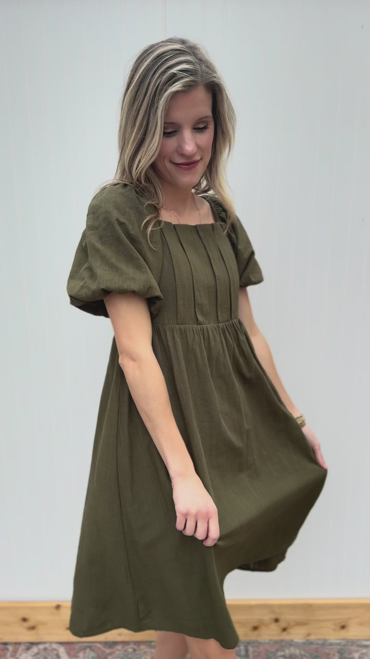 Video of Model wearing a textured olive knee length dress with a square neck and short sleeves.