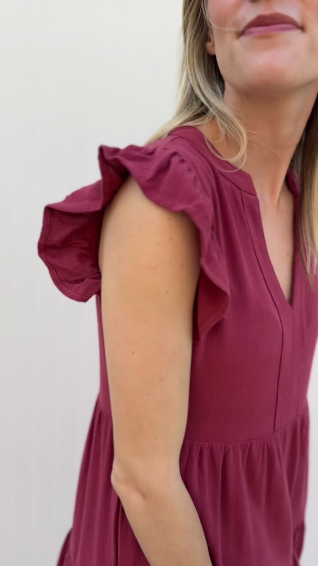 Video of Model wearing a maroon knee length dress with a v-neck and ruffle cap sleeves.