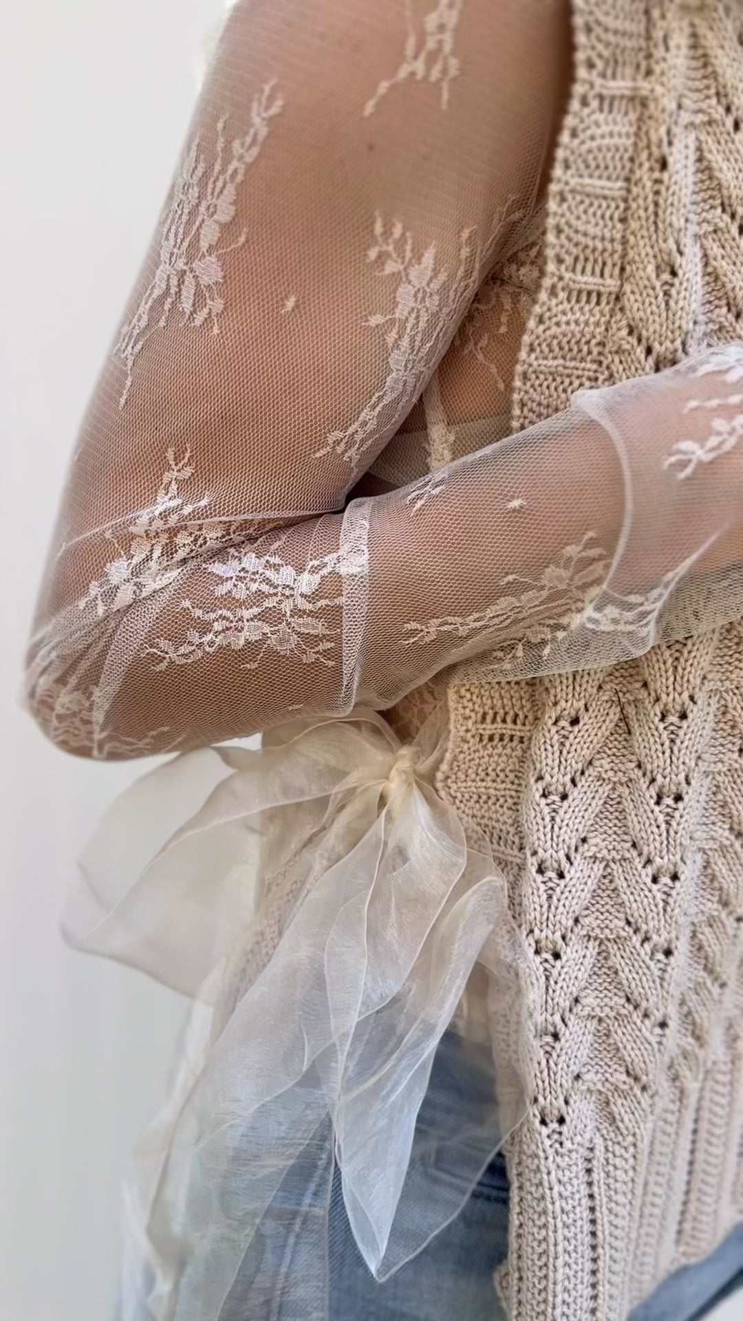 Video of Model wearing an oatmeal sleeveless, v-neck with ribbon side tie closures. 