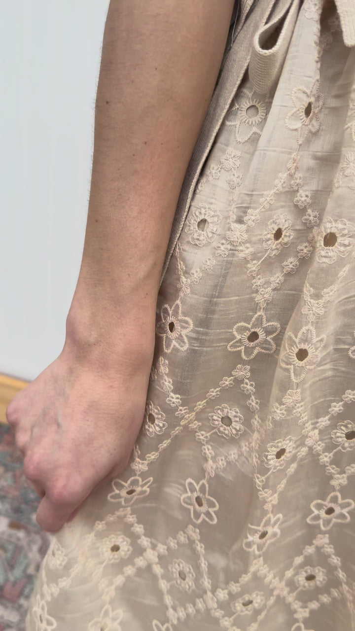 Video of Model wearing a pale coffee cut lace dress with attached sweater vest with side ties. 