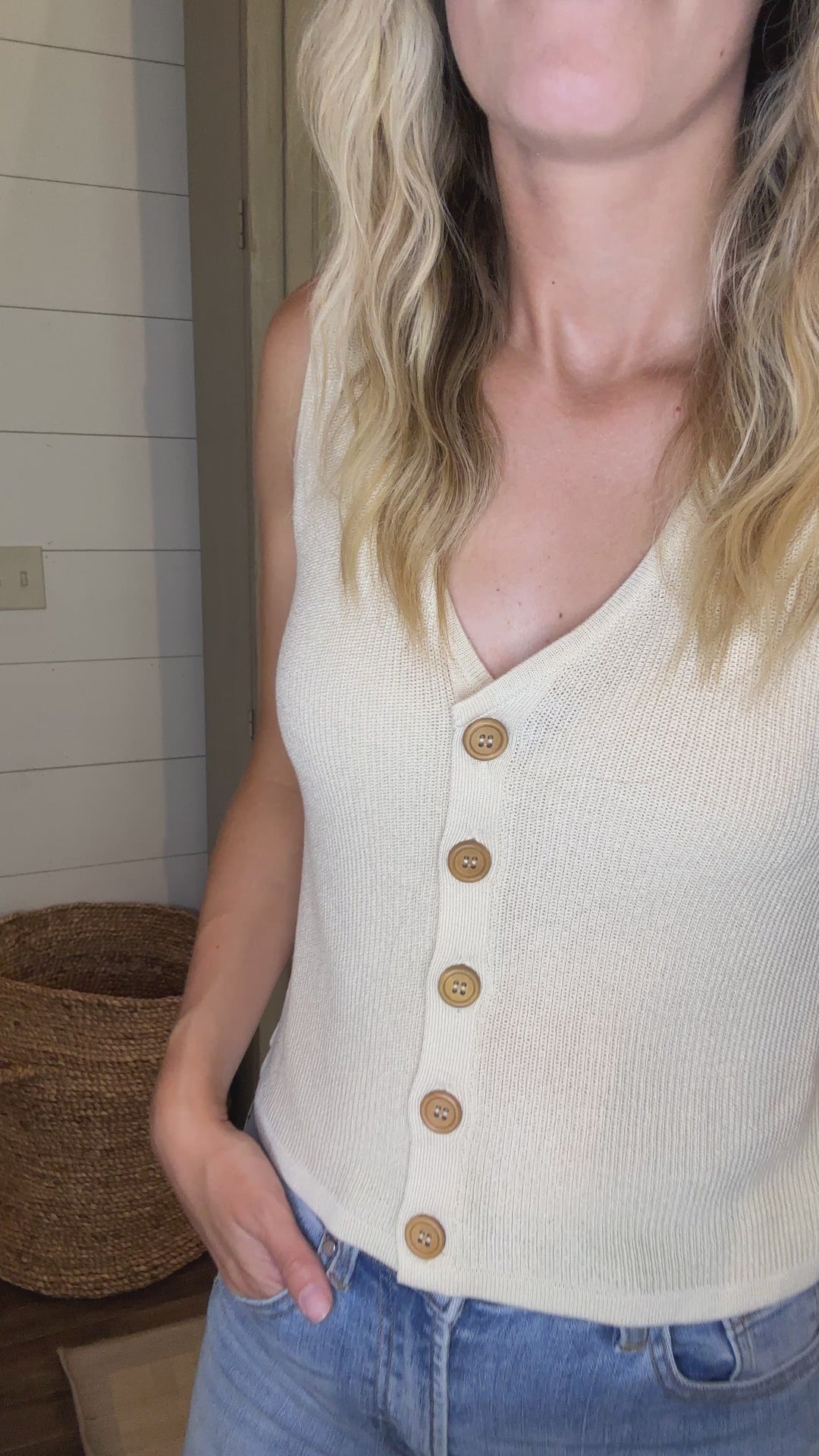 Video of Model wearing a cream knit sweater with a sleeveless design, v-neck and button front. 