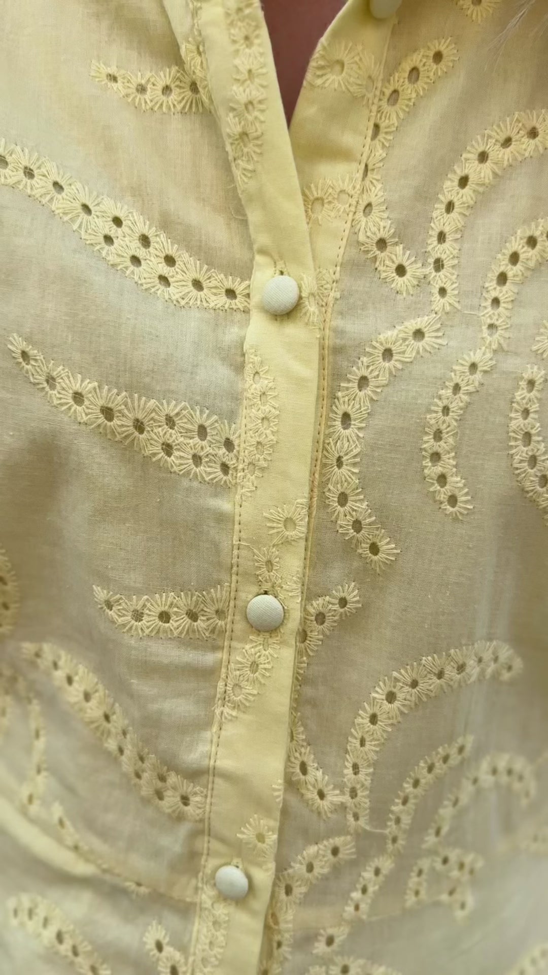 Video of Model wearing a yellow button up dress with eyelet overlay and bubble short sleeves. 