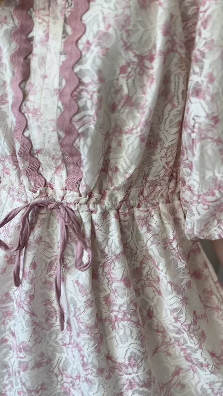 Video of Model wearing a cream dress with lace overlay with blush floral and 3/4 bubble sleeves.