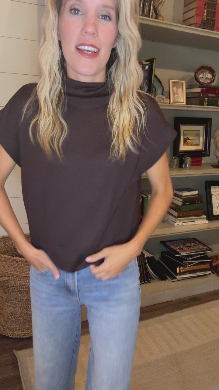 Video of Model wearing a mocha lightweight sweater with extended sleeves and a mock neck.  