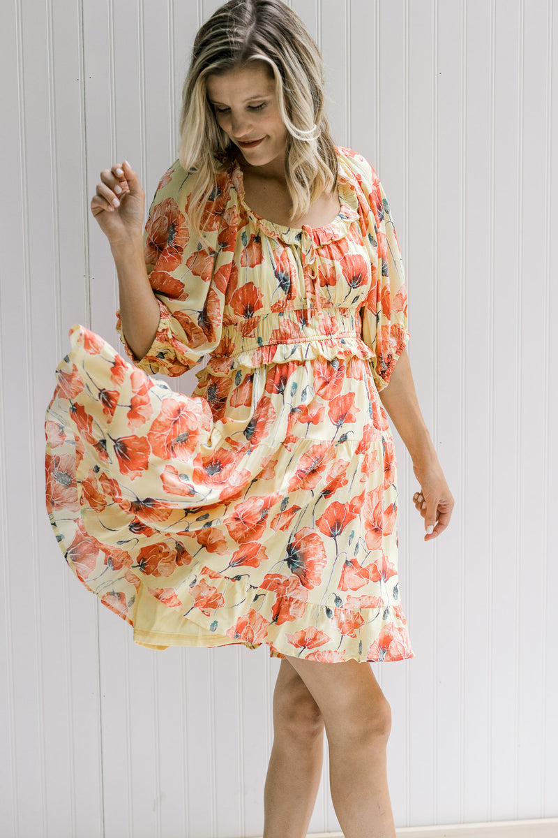 Model wearing a yellow above the knee dress with a coral floral pattern and an elastic waist. 