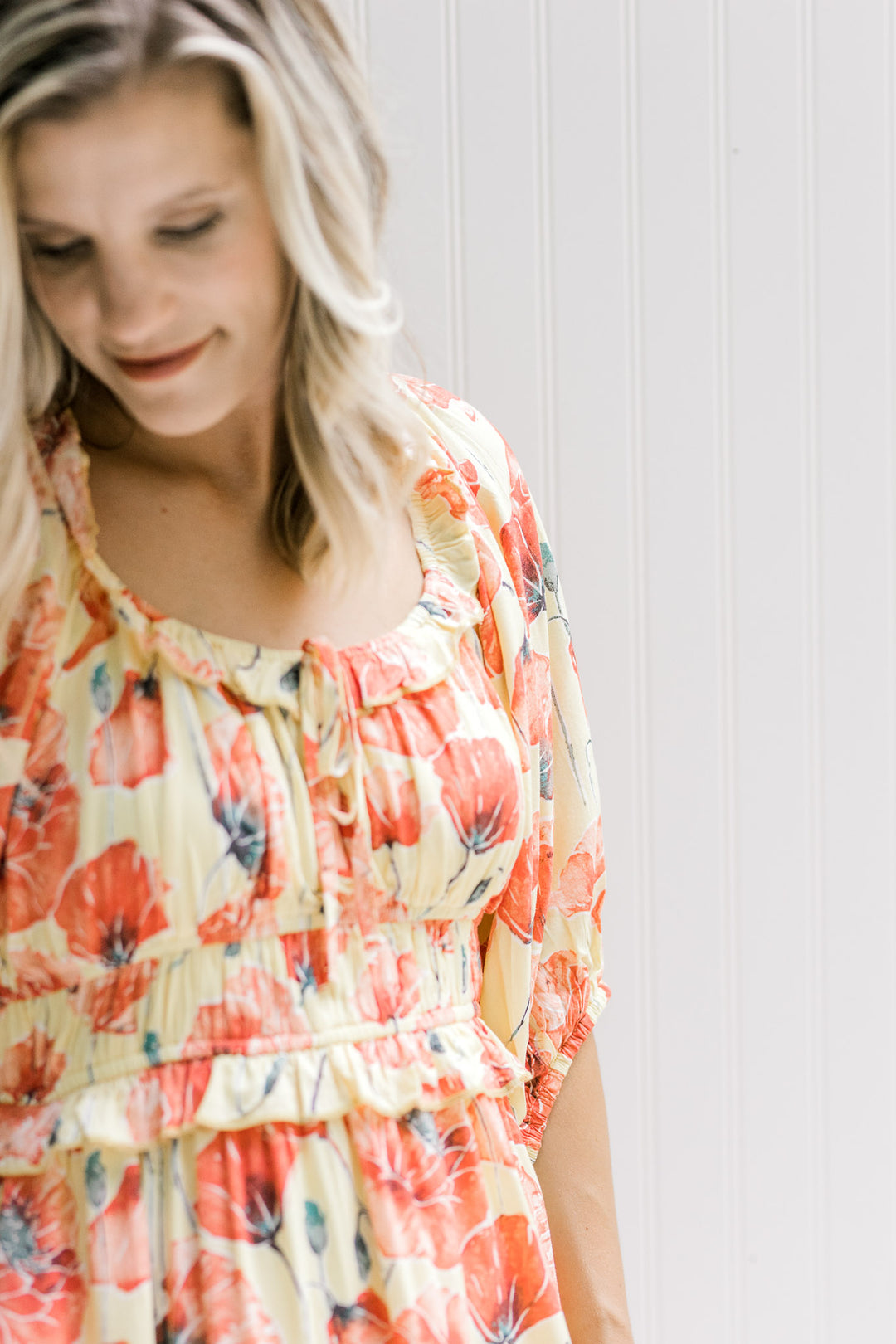 Close up of elastic waistband and round neck with tie on a yellow dress with coral floral pattern. 