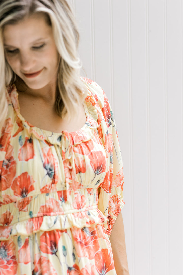 Close up of elastic waistband and round neck with tie on a yellow dress with coral floral pattern. 