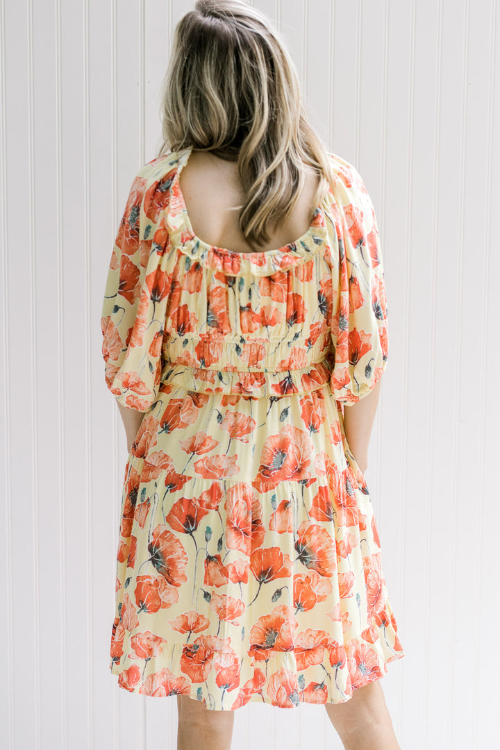 Back view of Model wearing a yellow dress with a coral floral pattern and an elastic waist.