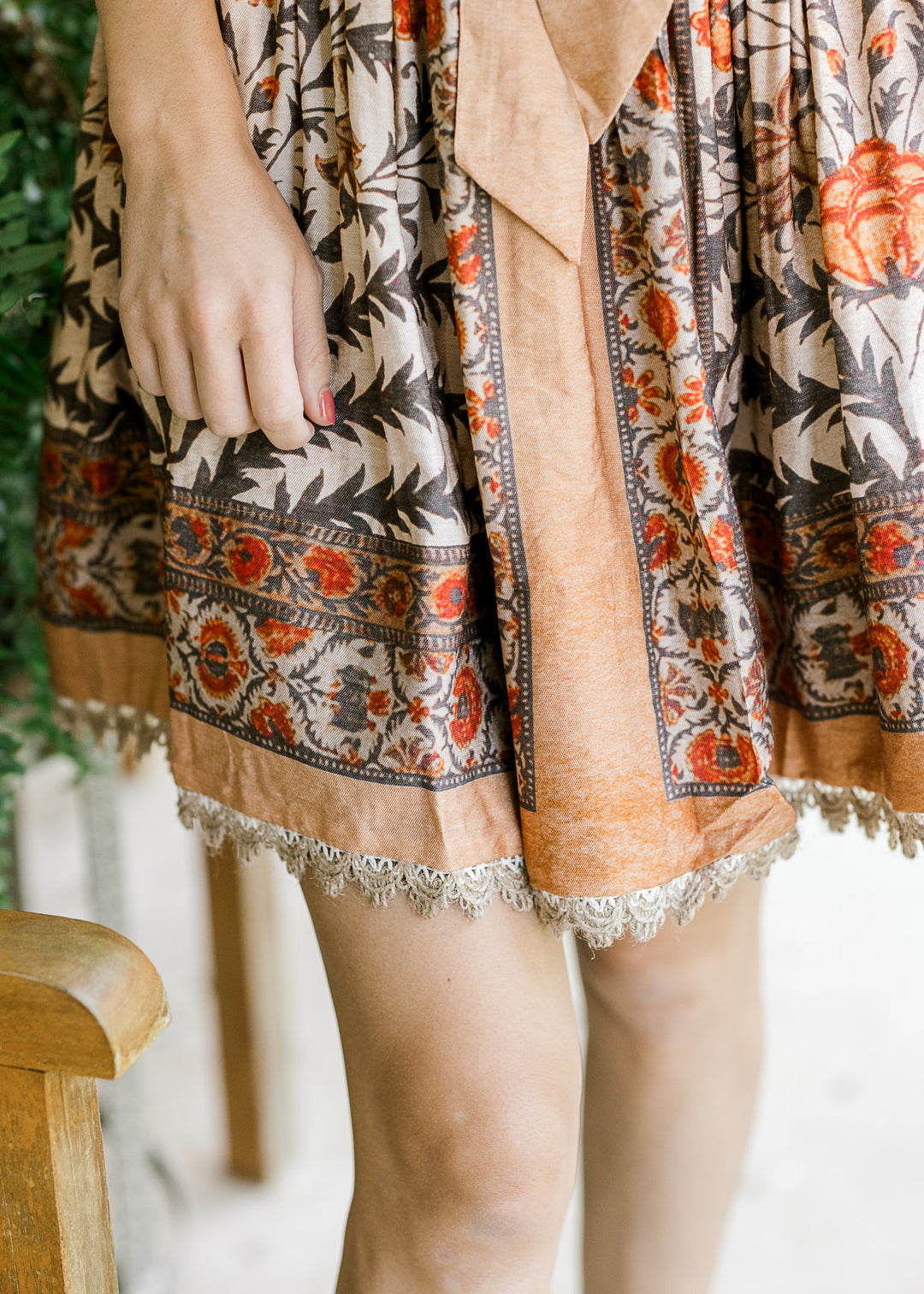 Close up of burlap lace at the hem of a cream dress with orange, tan and brown floral.