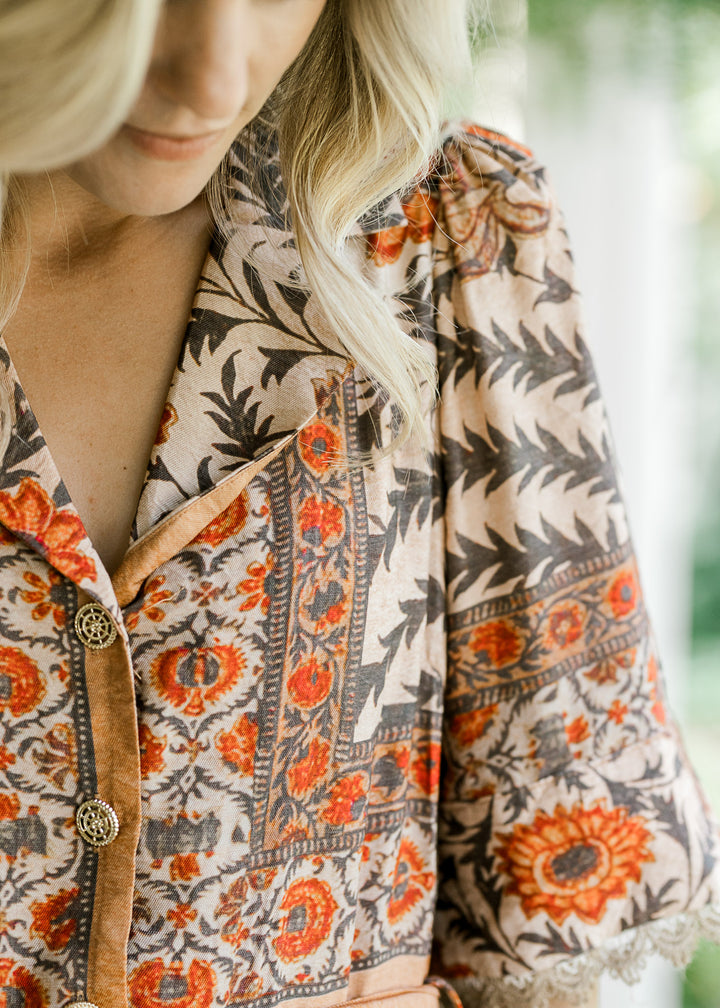 Close up of v-neck with a collar, pleated shoulder and buttons on a cream dress with floral. 