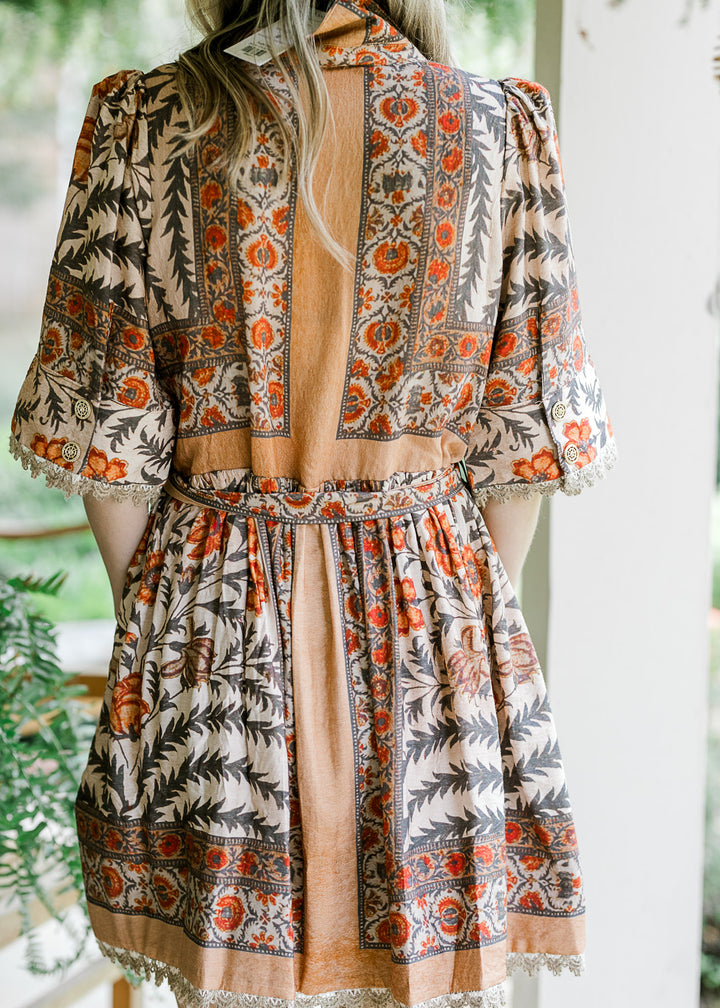 Back view of Model wearing a tan dress  with a floral design v-neck, short sleeves and tie waist. 
