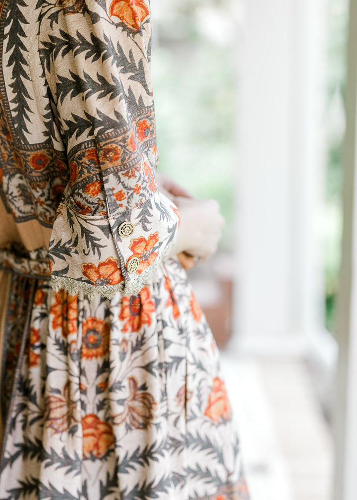 Close up of short sleeve (to elbow) with gold buttons and burlap lace on a cream floral dress. 