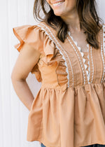 Close up of white scallop lace on a dusty orange babydoll top with ruffle cap sleeve. 