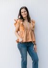 Model wearing jeans with a dusty orange top with ruffle cap sleeve and scallop white detail. 