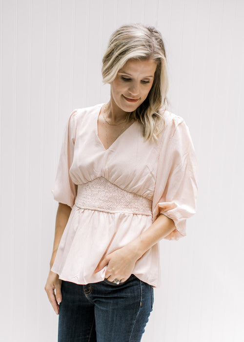 Model wearing a blush colored top with a cinched waist, v-neck and 3/4 bubble sleeves. 