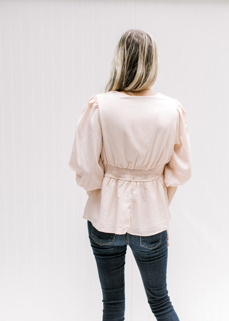 Back view of Model wearing a blush colored top with a cinched waist, v-neck and 3/4 bubble sleeves. 