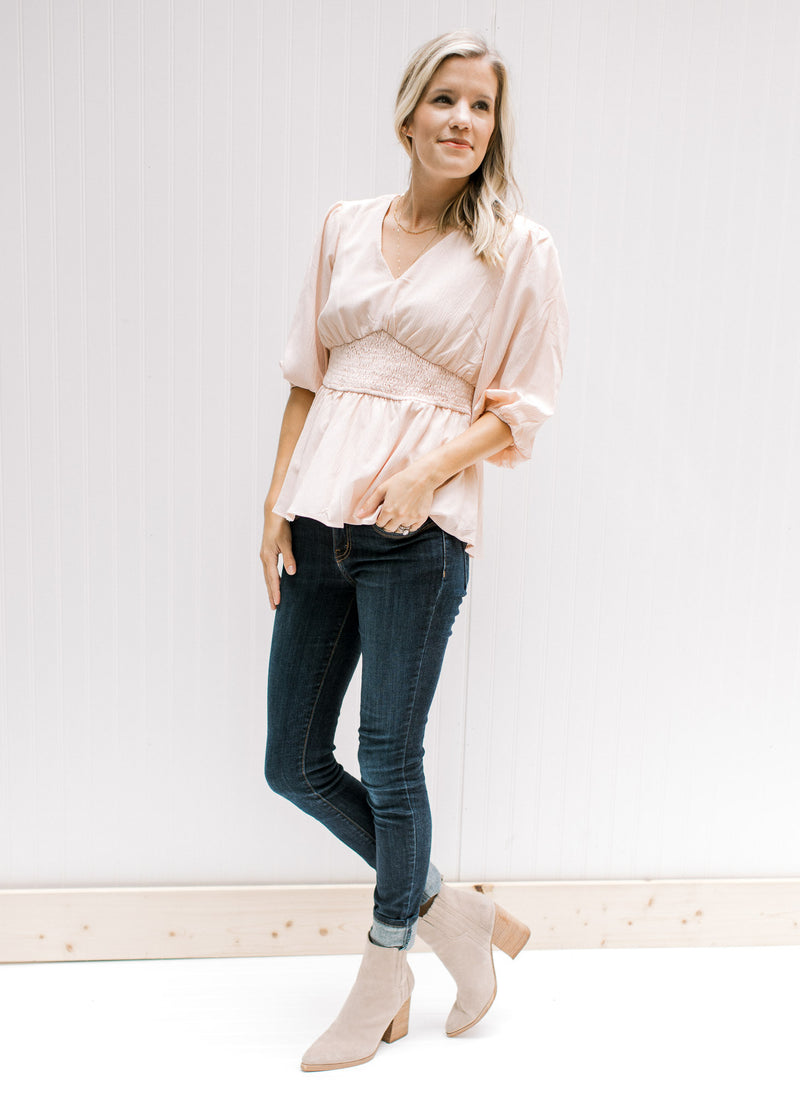 Model wearing jeans and booties with a blush colored top with a cinched waist and 3/4 sleeves. 