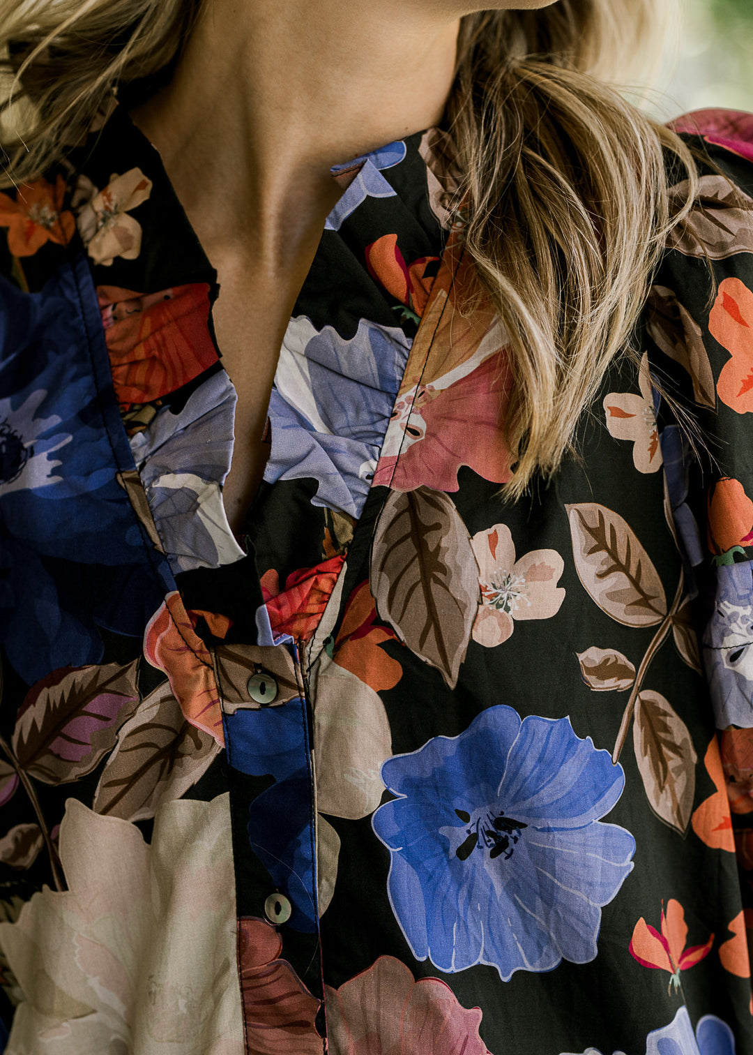 Close up of ruffle v-neck and buttons on a black dress with blue, pink and brown floral. 