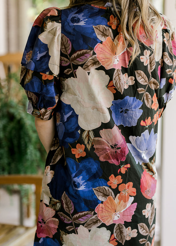 Back view of Model wearing a black dress with floral print, button front and short sleeves. 