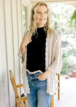 Model wearing a neutral open weave cardigan with scalloped hem and 3/4 sleeves. 