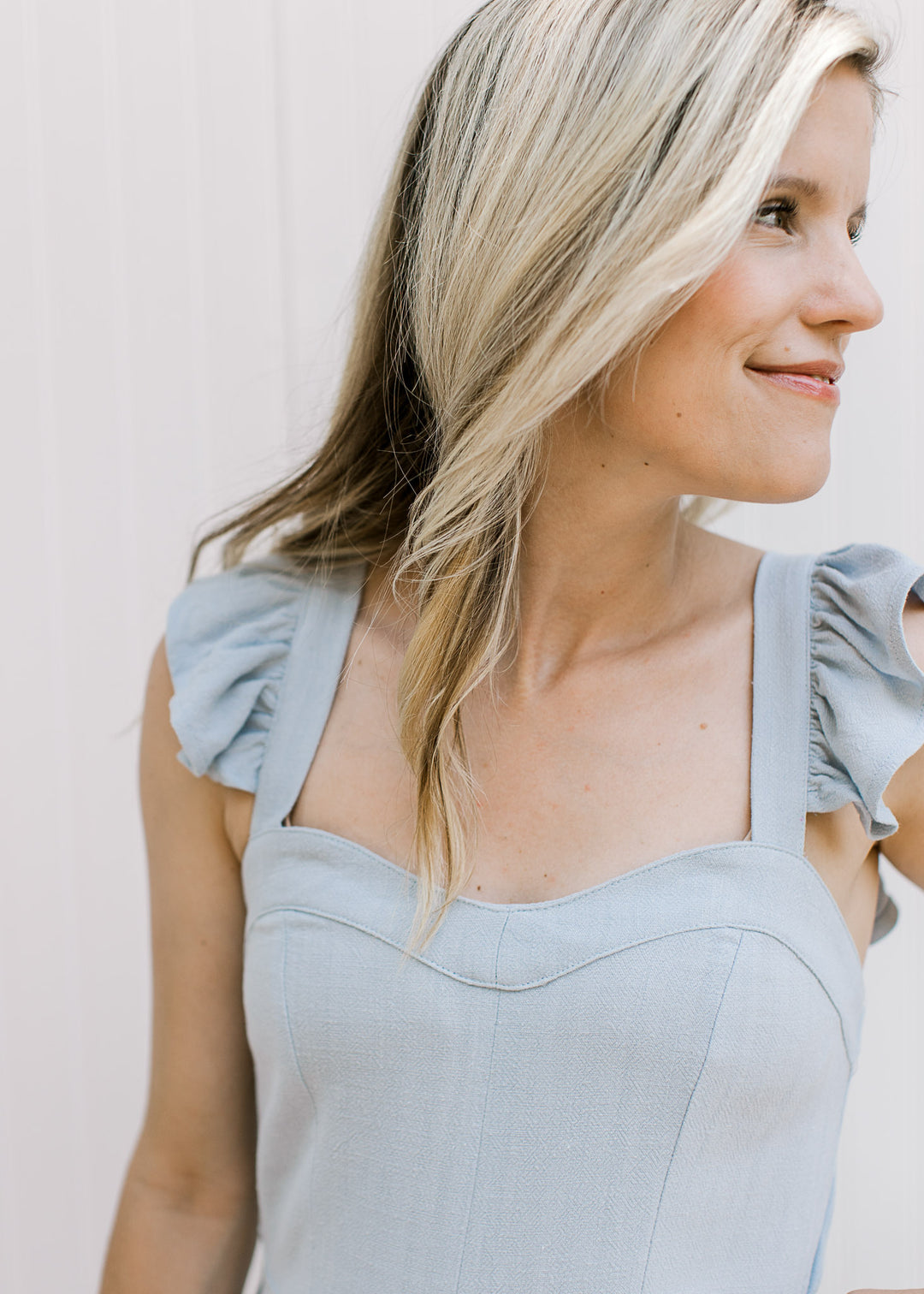 Close up of sweetheart neckline and ruffle straps on a light blue jumpsuit with wide legs. 