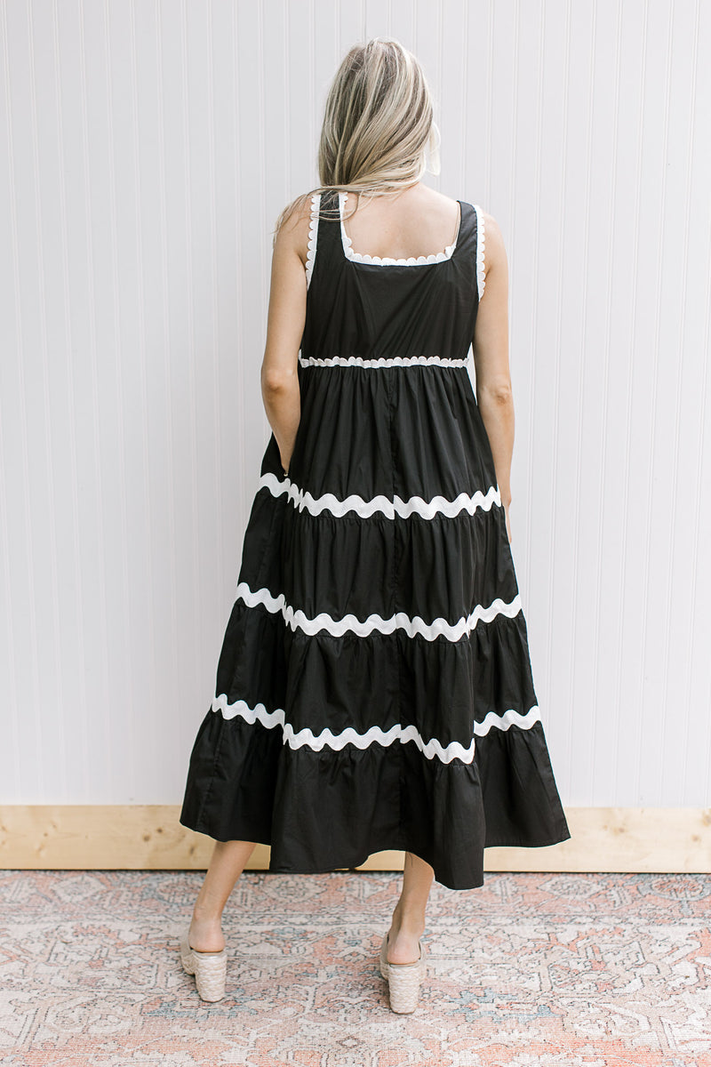 Back view of Model wearing a sleeveless black dress with white stripes and a square neck.