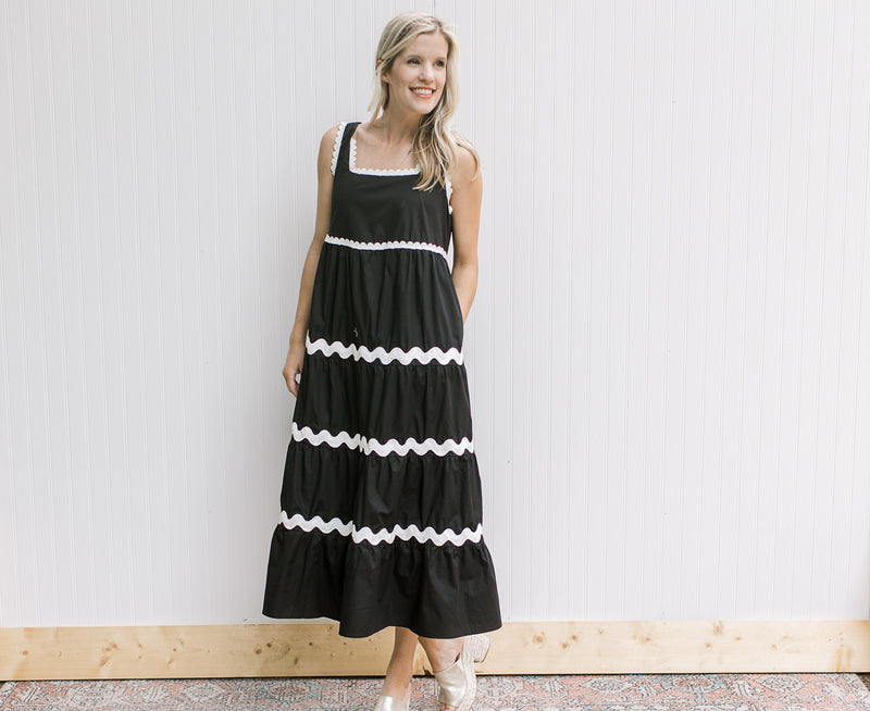 Model wearing a black maxi with white stripe detail, pockets and a square neck.