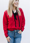 Model wearing a red knit sweater with black tie bow at v-neck and long sleeves. 