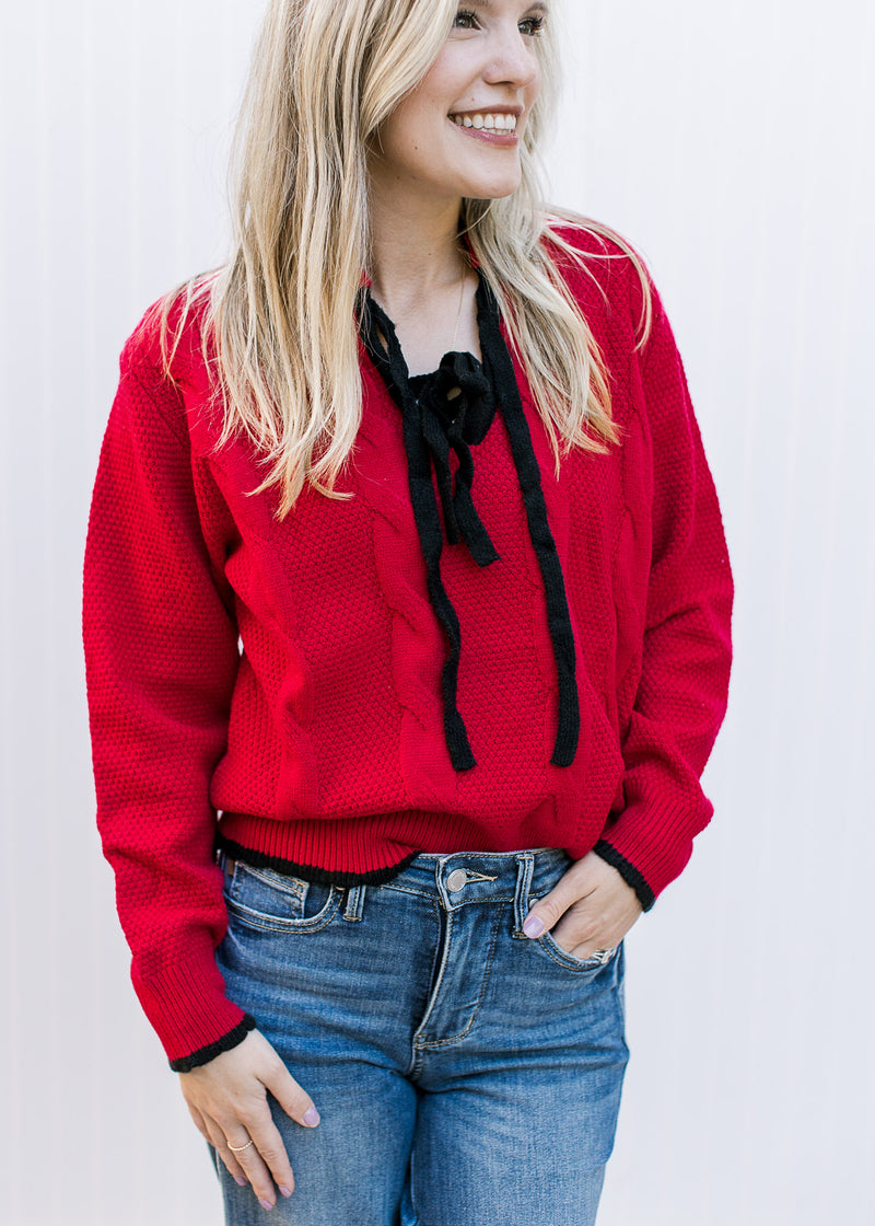 Model wearing a red knit sweater with black tie bow at v-neck and long sleeves. 