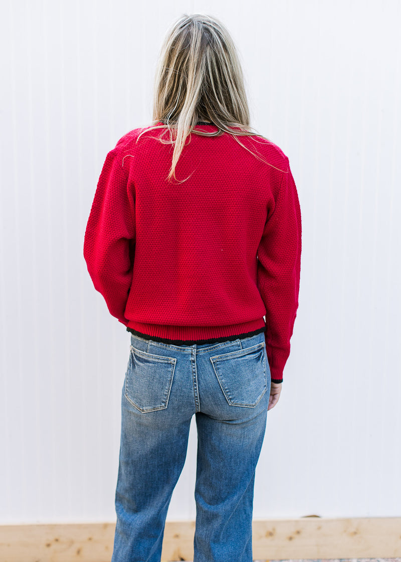 Back view of Model wearing a red knit sweater with black tie bow at v-neck and long sleeves. 