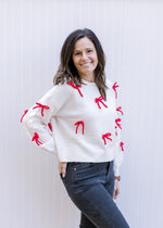 Side view of Model wearing a cream sweater adorned with red 3D bows and long sleeves.