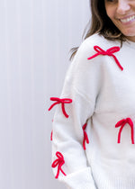 Close up of sleeve with red 3D bows and extended shoulder on a cream sweater. 