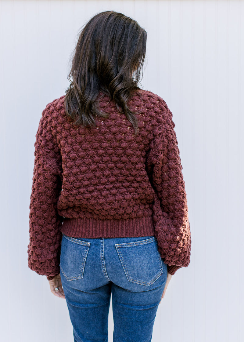 Back view of Model wearing a wine open knit sweater with bubble long sleeves and round neck.