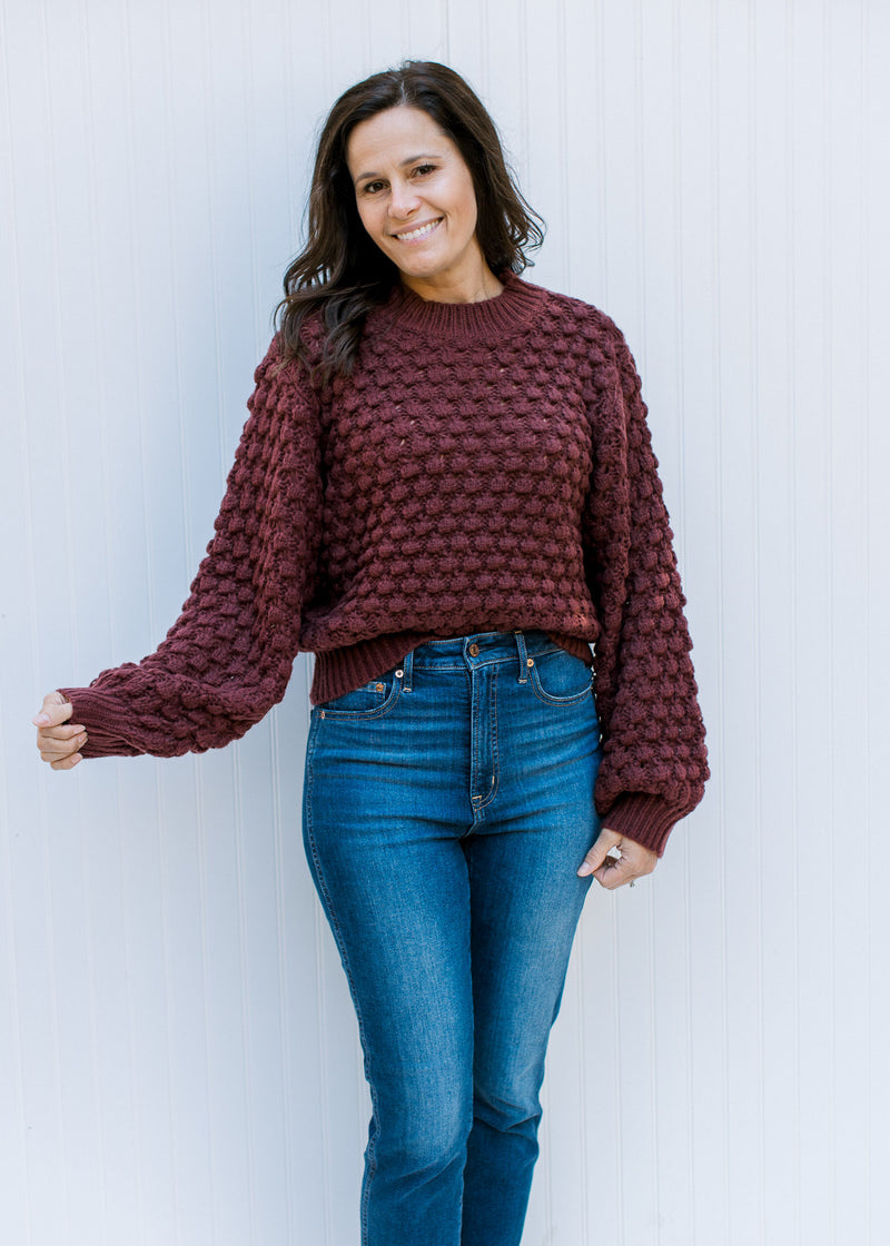 Model wearing jeans and a wine open knit sweater with bubble long sleeves and a round neck.